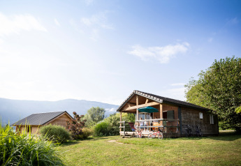 Chalet Montana, een houten hut met veranda en fietsen, omgeven door natuur bij Huttopia Lac d’Aiguebelette, Frankrijk.
