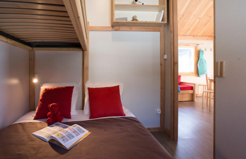 Hyggelig hytte-soveværelse med køjesenge, røde puder, børnebog og udsigt til stue i Chalet Montana.