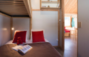 Hyggelig hytte-soveværelse med køjesenge, røde puder, børnebog og udsigt til stue i Chalet Montana.