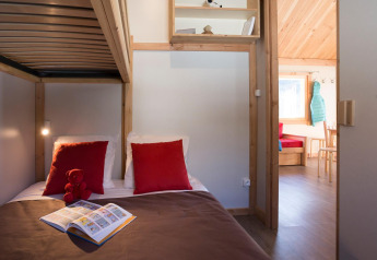 Knusse hut-slaapkamer met stapelbed, rode kussens, kinderboek en uitzicht op de woonkamer in Chalet Montana.