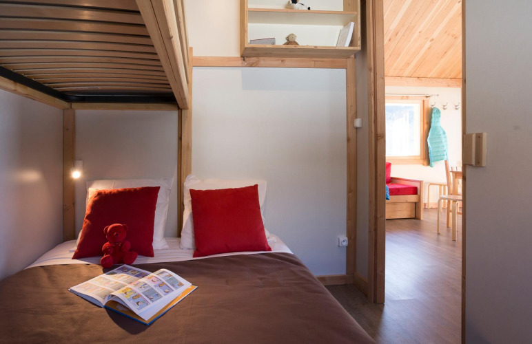 Dormitorio acogedor en cabaña con literas, cojines rojos, libro infantil y vista a la sala en Chalet Montana.