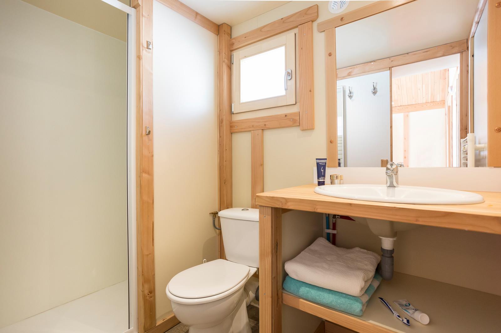 Lichte badkamer met houten kozijnen, douche, toilet en wastafel in Chalet Montana, Huttopia Lac d'Aiguebelette, Frankrijk.