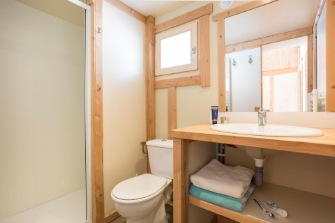 Lichte badkamer met houten kozijnen, douche, toilet en wastafel in Chalet Montana, Huttopia Lac d’Aiguebelette, Frankrijk.