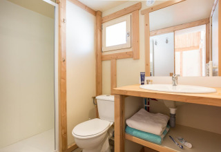 Lyst badeværelse med trærammer, bruser, toilet og vask på Chalet Montana, Huttopia Lac d’Aiguebelette, Frankrig.