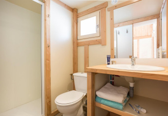 Bagno luminoso con telai in legno, doccia, WC e lavandino presso Chalet Montana, Huttopia Lac d’Aiguebelette, Francia.