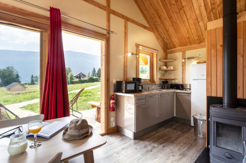 Vista interior del Chalet Montana en Huttopia Lac d’Aiguebelette, Francia, con cocina y paisaje exterior natural.