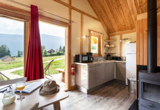 Vista interior del Chalet Montana en Huttopia Lac d’Aiguebelette, Francia, con cocina y paisaje exterior natural.