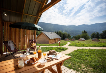 Uitzicht vanuit Chalet Montana bij Huttopia Lac d’Aiguebelette in Frankrijk met huisjes, bergen en ontbijt buiten.