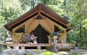 To personer slapper af foran en safari-telt 'Tente Trappeur' i en skov ved Huttopia Lac d’Aiguebelette, Frankrig.
