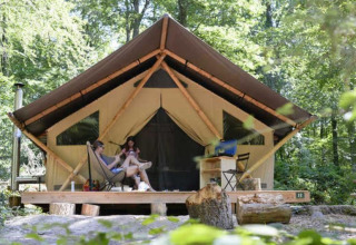 Dos personas se relajan frente a una tienda safari llamada Tente Trappeur en Huttopia Lac d’Aiguebelette, Francia.