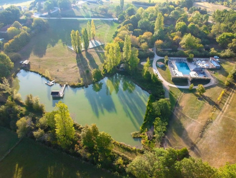 Luftfoto af Huttopia Vallée du Lot feriepark i Nouvelle-Aquitaine, Frankrig, med sø, pool og grønne træer.