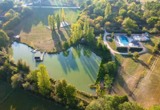 Luftfoto af Huttopia Vallée du Lot feriepark i Nouvelle-Aquitaine, Frankrig, med sø, pool og grønne træer.