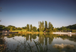 Vista panoramica di un lago tranquillo con alberi e prati a Huttopia Vallée du Lot, Nouvelle-Aquitaine, Francia.