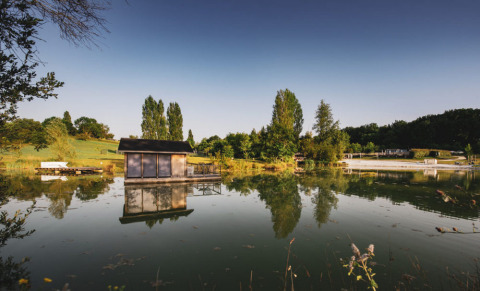 Reflejo de una cabaña sobre el lago en el parque Huttopia Vallée du Lot, Nouvelle-Aquitaine, Francia, al atardecer.