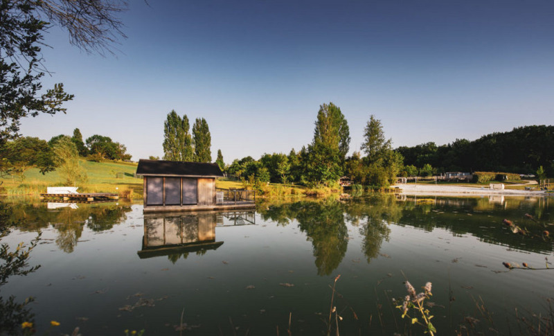 Weerspiegeling van een hut aan het meer in Huttopia Vallée du Lot vakantiepark, Nouvelle-Aquitaine, Frankrijk.