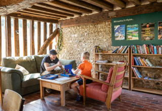 Due persone giocano a un gioco da tavolo in un’area lounge accogliente a Huttopia Vallée du Lot, Francia.