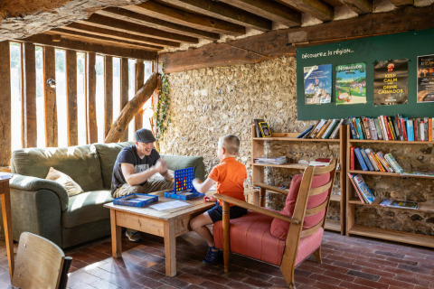 Zwei Personen spielen ein Brettspiel in einer gemütlichen Ecke mit Büchern bei Huttopia Vallée du Lot, Frankreich.