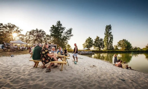 Menschen entspannen am Sandstrand von Huttopia Vallée du Lot in Nouvelle-Aquitaine, Frankreich am Wasser.