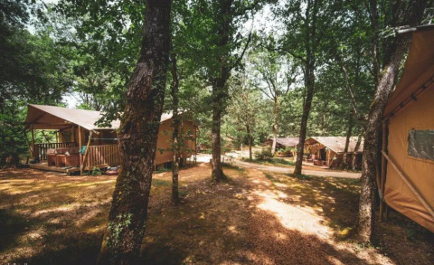 Tiendas tipo lodge entre árboles en Huttopia Vallée du Lot, parque vacacional en Nouvelle-Aquitaine, Francia.