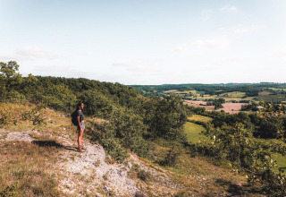 A hiker with a backpack stands overlooking lush hills and farmland at Huttopia Vallée du Lot in France.
