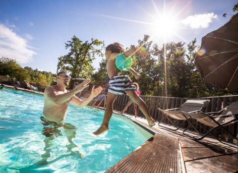 Un père joue avec son enfant dans la piscine sous le soleil au Huttopia Vallée du Lot, en Nouvelle-Aquitaine, France.