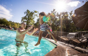 Un padre gioca con il figlio in piscina al sole presso Huttopia Vallée du Lot, villaggio vacanze in Nouvelle-Aquitaine.