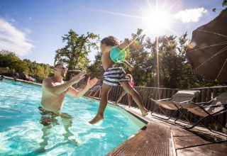 Un padre gioca con il figlio in piscina al sole presso Huttopia Vallée du Lot, villaggio vacanze in Nouvelle-Aquitaine.