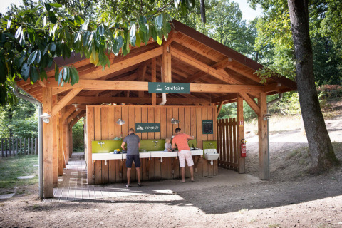 Área sanitaria de madera al aire libre, personas lavando platos en un camping de vacaciones en Francia.