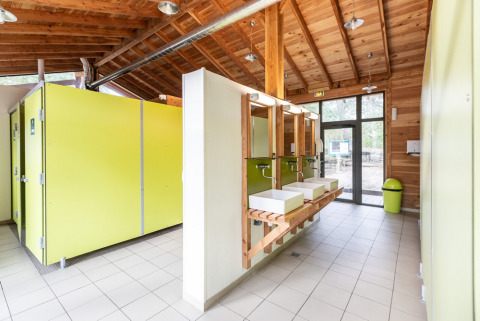 Bagno pubblico moderno e luminoso con cabine verdi e soffitto in legno a Huttopia Vallée du Lot, Francia.