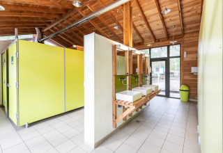 Bagno pubblico moderno e luminoso con cabine verdi e soffitto in legno a Huttopia Vallée du Lot, Francia.