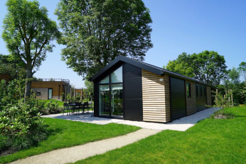 Moderne Velthorst-lodge met grote ramen en houten gevel, gelegen in een groene tuin met bomen.