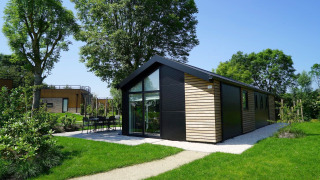 Moderna cabaña Velthorst con ventanales y revestimiento de madera, rodeada de césped y árboles verdes.