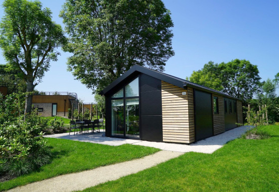 Moderne Velthorst-lodge met grote ramen en houten gevel, gelegen in een groene tuin met bomen.