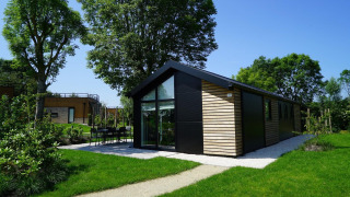 Moderna cabaña Velthorst con ventanales y revestimiento de madera, rodeada de césped y árboles verdes.