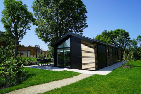 Lodge Velthorst moderne avec baies vitrées et bardage bois, entourée de jardin vert et d’arbres.