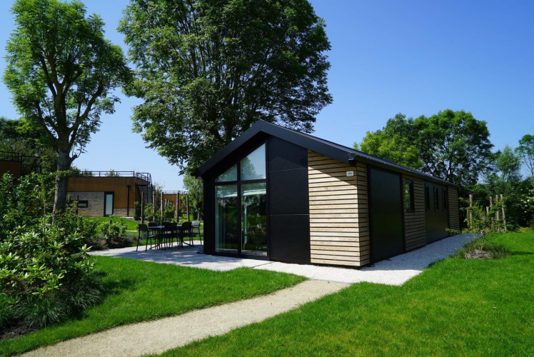 Moderne Velthorst-Lodge mit Holzverkleidung und großen Fenstern, umgeben von Grün und Bäumen.