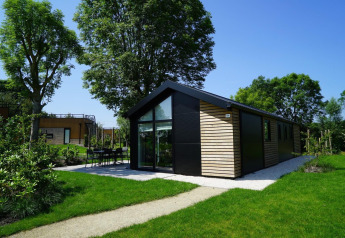 Lodge Velthorst moderne avec baies vitrées et bardage bois, entourée de jardin vert et d’arbres.