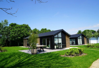 Moderni lodge Velthorst a Kagerplassen nei Paesi Bassi, circondati da prato verde e alberi sotto cielo blu.