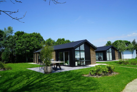 Lodges Velthorst modernes à Kagerplassen, Pays-Bas, entourés de pelouses vertes et d'arbres sous un ciel bleu.