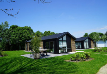 Lodges Velthorst modernes à Kagerplassen, Pays-Bas, entourés de pelouses vertes et d'arbres sous un ciel bleu.