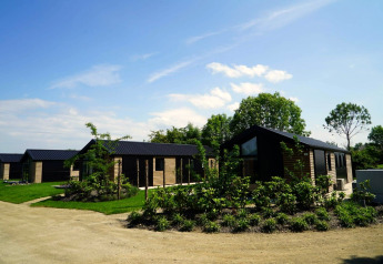 Lodges Velthorst al Kagerplassen nei Paesi Bassi, con cabine in legno moderne e tanto verde sotto il cielo azzurro.