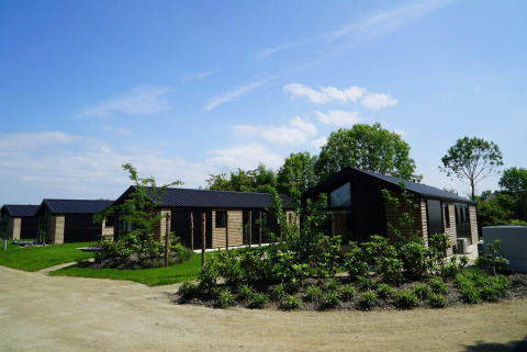 Lodges Velthorst al Kagerplassen nei Paesi Bassi, con cabine in legno moderne e tanto verde sotto il cielo azzurro.