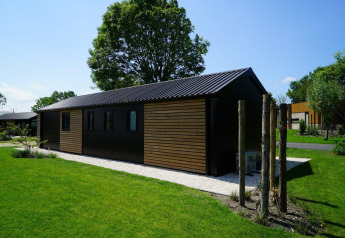 Moderna cabaña Velthorst en Kagerplassen, Países Bajos, rodeada de césped verde y frondosos árboles.