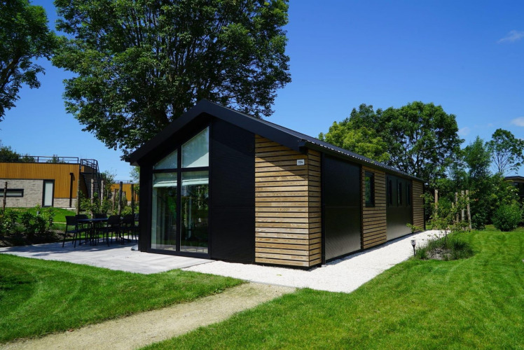 Velthorst-Lodge am Kagerplassen in den Niederlanden, umgeben von grüner Wiese und Bäumen bei Sonnenschein.