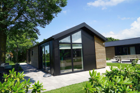 Moderne lodge met houten gevel en grote ramen bij Kagerplassen in Nederland, omgeven door groen.
