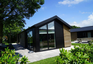 Moderna cabaña con revestimiento de madera y grandes ventanales en Kagerplassen, Países Bajos, rodeada de naturaleza.