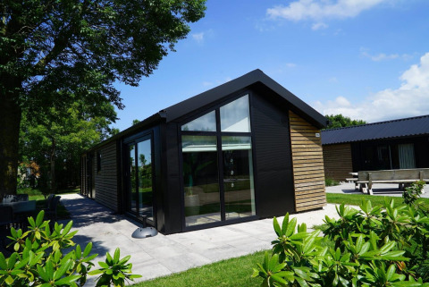 Lodge moderne avec bardage en bois et grandes fenêtres à Kagerplassen, Pays-Bas, entouré de verdure.