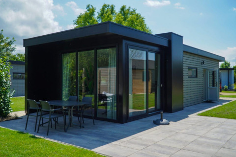 Moderne Lodge namens Cube la Mer Wellness mit großen Glasfenstern, Terrasse und grüner Landschaft.