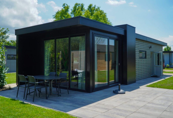 Moderne Lodge namens Cube la Mer Wellness mit großen Glasfenstern, Terrasse und grüner Landschaft.