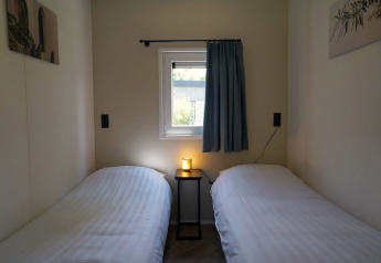 Two single beds with white sheets, small table with light, and window in Cube la Mer Wellness, Kagerplassen.